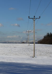 Electricity pylon on snow against sky