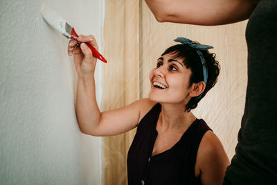 Portrait of smiling young woman holding hands against wall