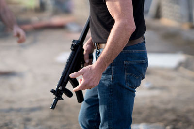 Midsection of man with rifle standing on ground