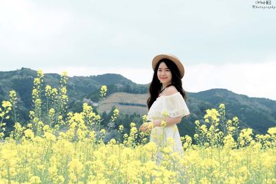 Full length of young woman standing against yellow flowering plants