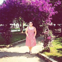 Portrait of woman standing by pink flowers against trees