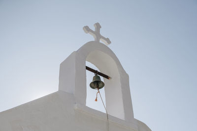 Low angle view of the bell and cross on a church in ana mera, mykonos, greece.