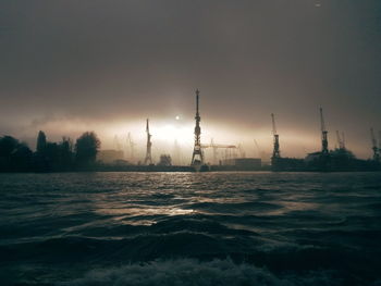 Silhouette cranes in city against sky during sunset