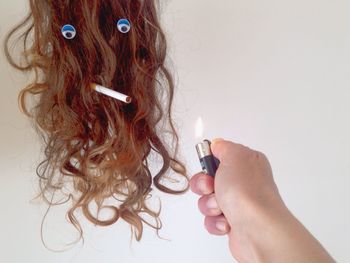 Cropped hand lighting cigarette in wig with anthropomorphic face