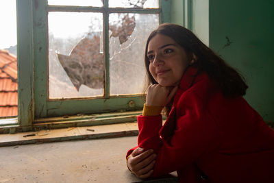 Portrait of woman looking away while sitting on window