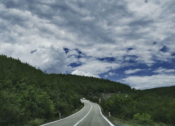 Country road amidst landscape against sky