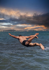 Full length of woman jumping in sea against sky during sunset