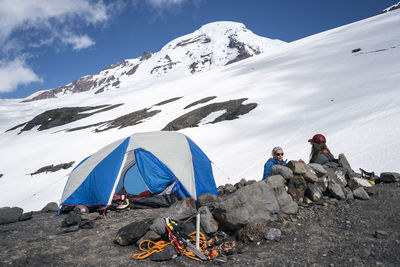 Two women mountaineers sit talking near tent on mount baker