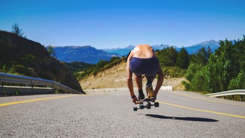 Rear view of man skateboarding on road against sky