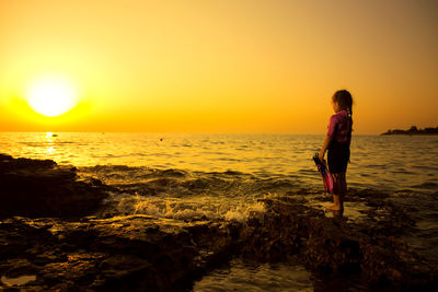 Side view of girl standing at beach against sky during sunset