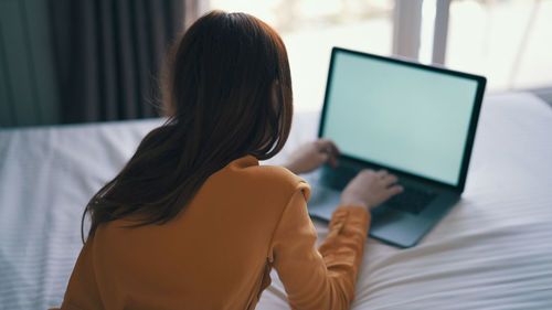 Rear view of woman using laptop at home