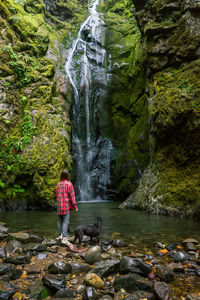 Young woman in flannel with dog looking at waterfall