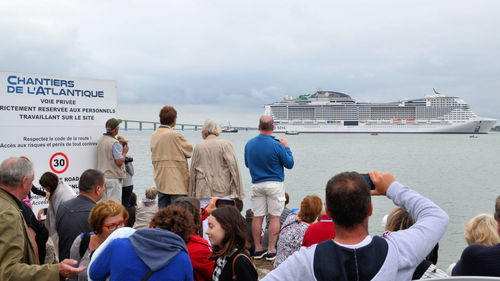 Rear view of people standing by boats against sky