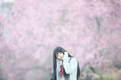 Portrait of young woman standing on pink cherry blossom