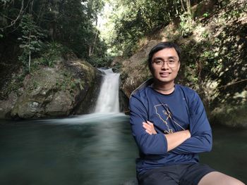 Portrait of young man standing against waterfall in forest
