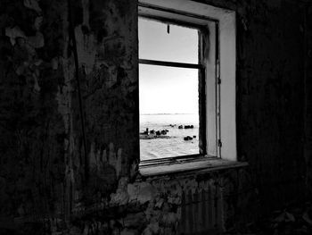 Window in abandoned building by sea against sky