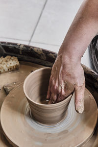 Hand of senior woman sculpting clay vase on potter's wheel.