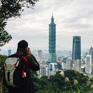 Rear view of man photographing cityscape against sky