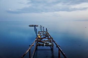 Abandoned pier on calm lake against cloudy sky