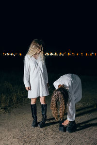 Full length of female friends wearing white dress standing on land at night