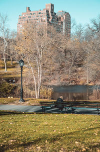 Park bench by lake against buildings in city