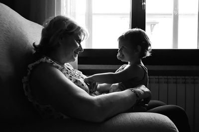 Mother looking at cute daughter while sitting on sofa at home