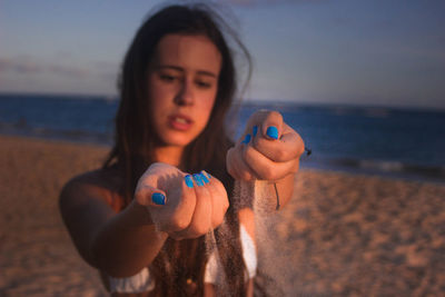 Teenage girl playing with sand at beach against sky