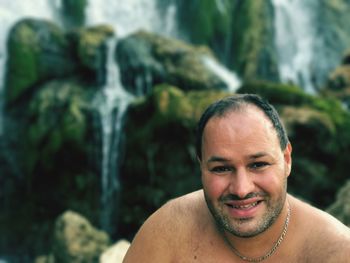 Portrait of shirtless happy man against waterfall