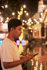 Side view of young man using mobile phone at night