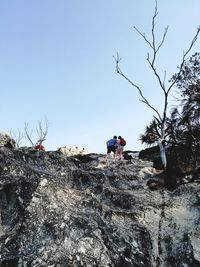 Low angle view of man and woman hiking on mountain against clear sky