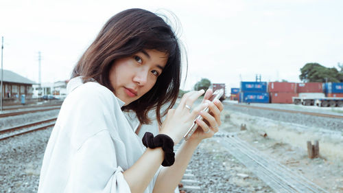 Portrait of beautiful young woman on railroad tracks against sky in city