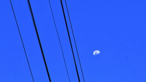 Low angle view of electricity pylon against clear blue sky