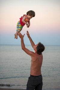 Full length of father and son holding while standing at beach