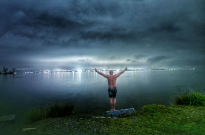 Rear view of man standing in sea against storm clouds