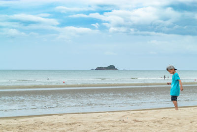 Boy playing on sand at beach against sky