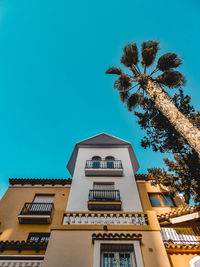 Low angle view of building and palm tree against blue sky