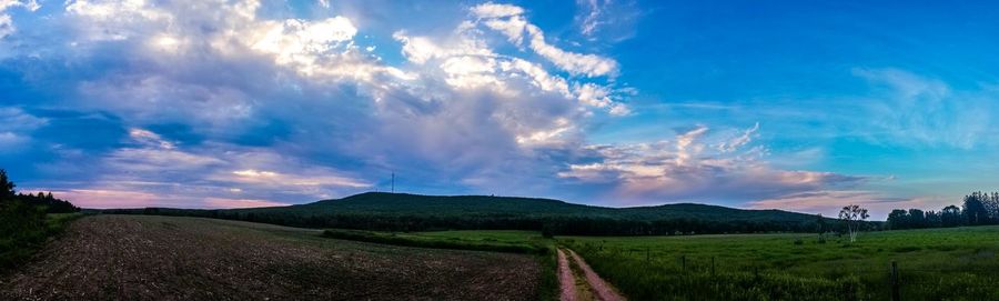 Country road on grassy field against cloudy sky
