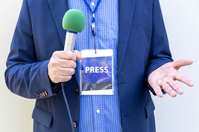 Male reporter with press pass at news conference or media event, holding microphone