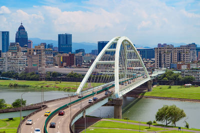 Bridge over river by buildings in city against sky