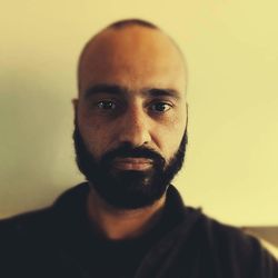 Close-up portrait of bearded man against wall at home