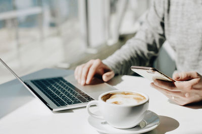 Midsection of man using laptop by coffee at table in cafe