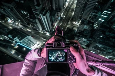 Midsection of man photographing illuminated cityscape at night