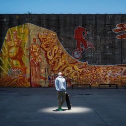 Man walking on footpath against graffiti wall