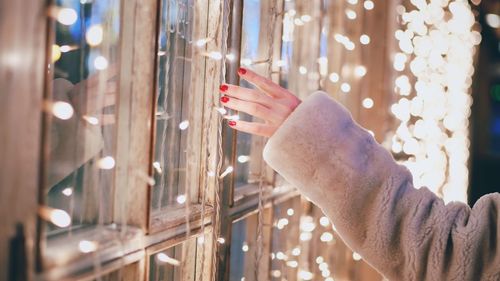 Close-up of woman hand touching illuminated lights on window