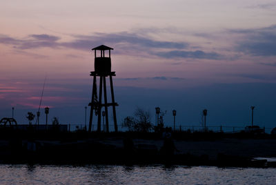 Silhouette water tower by sea against sky during sunset