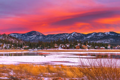 Scenic view of lake by snowcapped mountains against orange sky