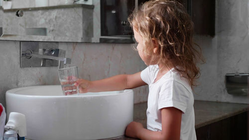 Side view of girl filling water in glass at sink