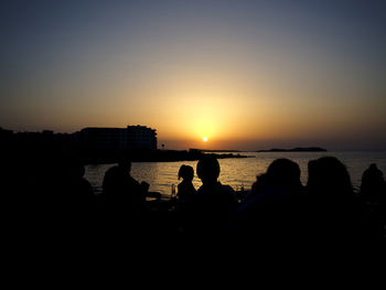 Silhouette people on sea against clear sky during sunset