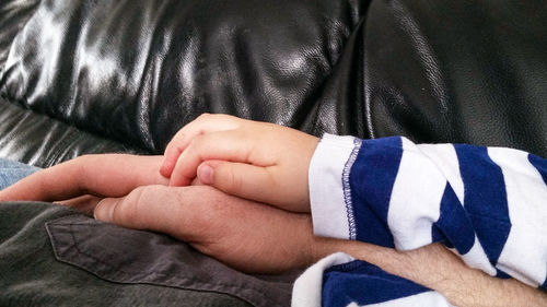 Cropped image of father with boy resting on sofa at home