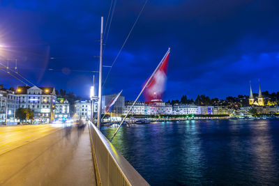 Illuminated city by river against sky at night